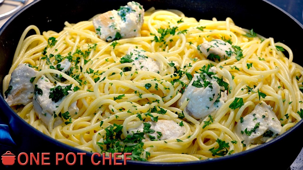 A close-up of a pan filled with spaghetti, tender chicken pieces, and garnished with fresh parsley.