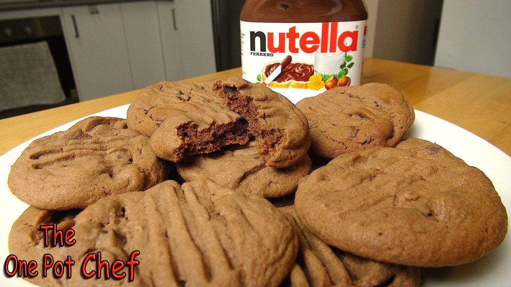 A plate of freshly baked Nutella cookies with a jar of Nutella in the background.
