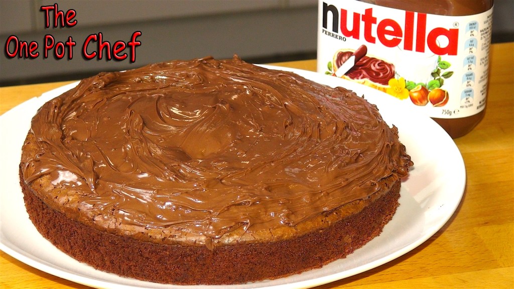 A round chocolate cake topped with a generous layer of Nutella, placed on a white plate with a wooden background.