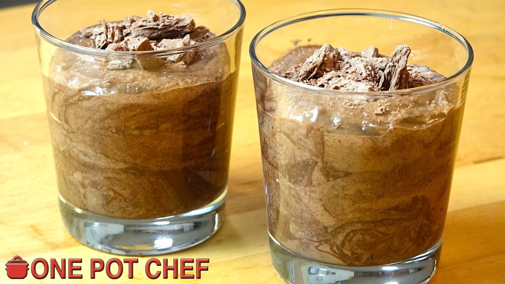 Two glasses of chocolate mousse topped with shavings of chocolate, placed on a wooden surface.