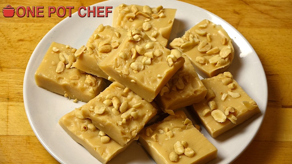 A plate of homemade peanut fudge pieces topped with chopped peanuts, placed on a wooden table.