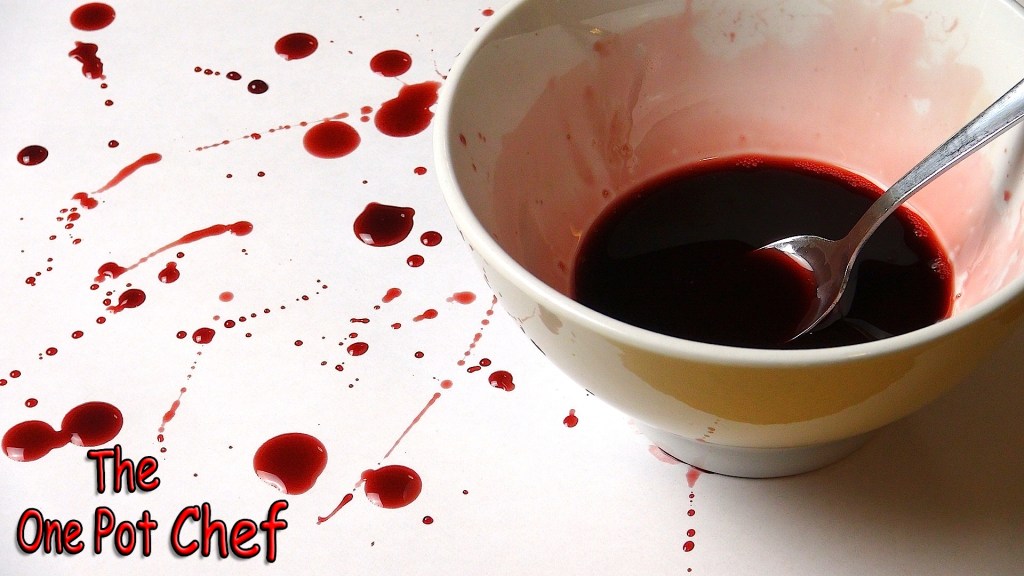 A white bowl containing dark red liquid, with splatters of the same liquid around it on a white surface, and a spoon resting inside the bowl.
