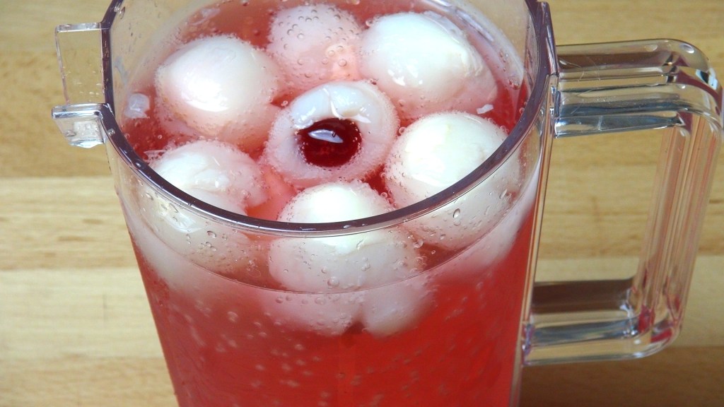 A clear jug filled with pink fizzy drink, featuring several white fruit balls and a cherry floating on top.