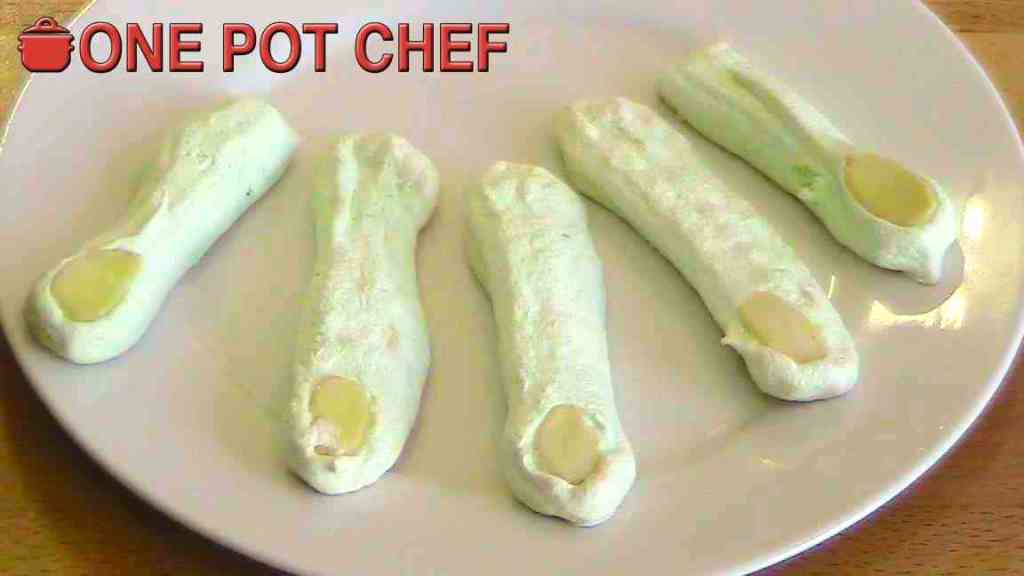 A plate featuring five green marshmallow-like fingers with a rounded almond tip, resembling spooky fingers for a Halloween treat.