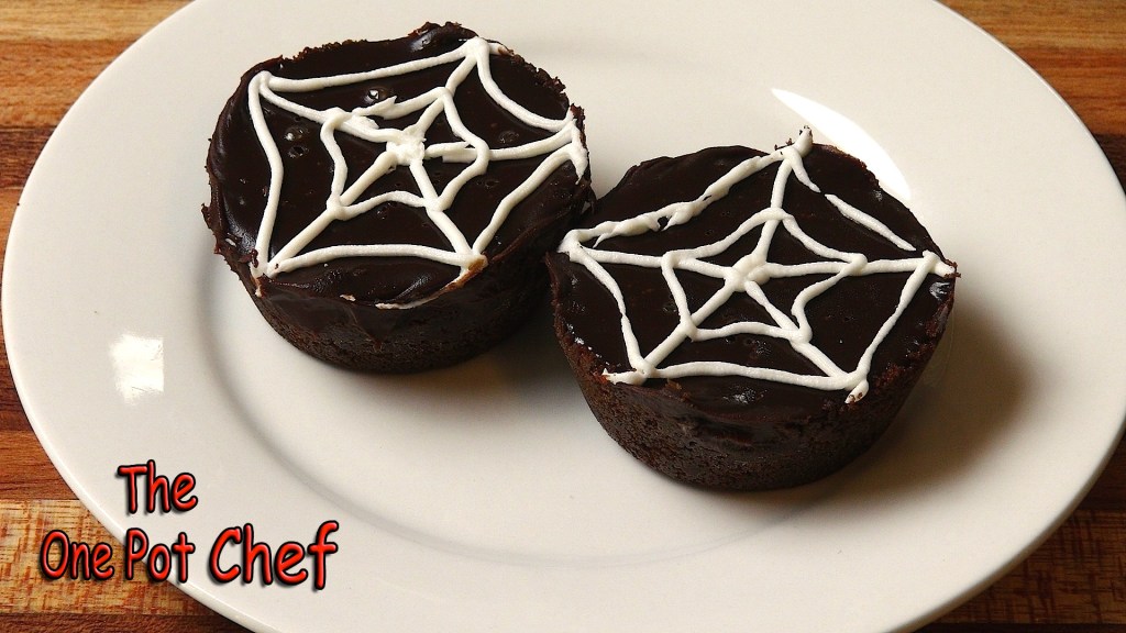 Two chocolate-covered cakes on a white plate, decorated with white icing in a spider web design.