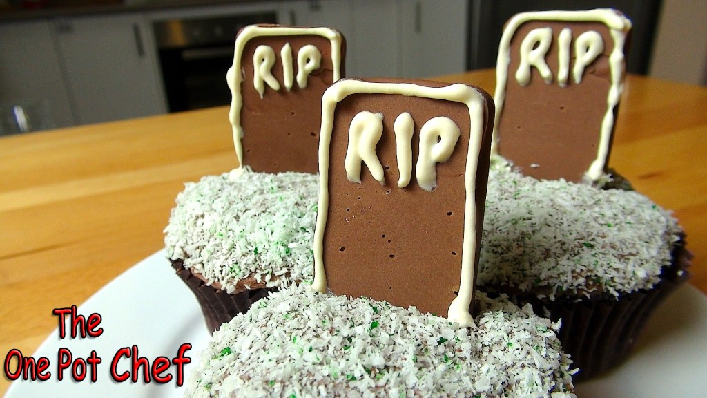 A plate of Halloween-themed cupcakes, topped with chocolate gravestones inscribed with 'RIP' and surrounded by coconut shavings resembling grass.