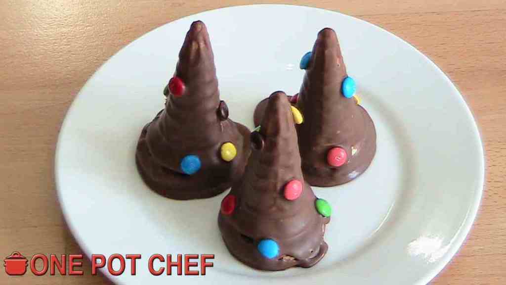 Three chocolate-covered cone-shaped desserts decorated with colourful candy buttons on a white plate.