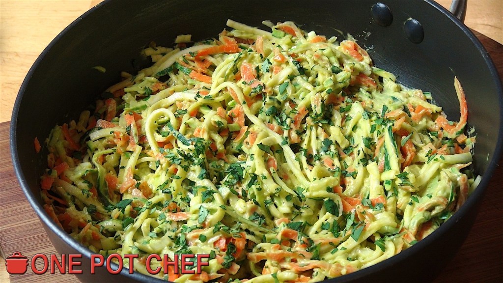 A large saucepan filled with a colourful mixture of shredded vegetables, including zucchini, carrots, and herbs, mixed together in a creamy dressing.